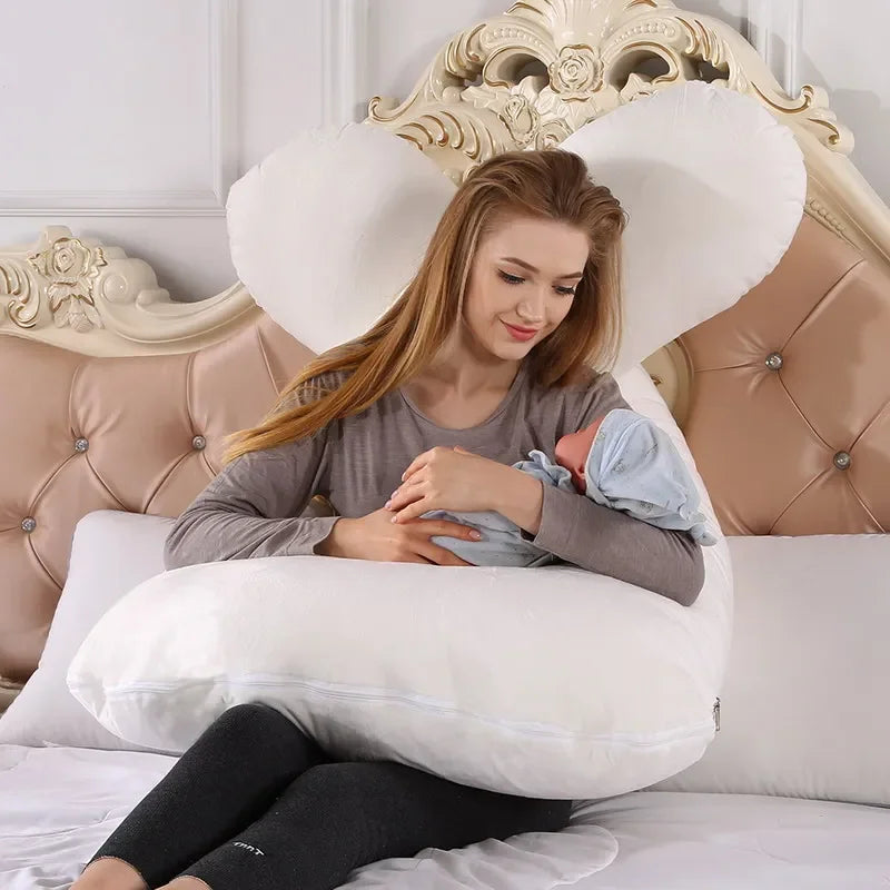 Mother holding a baby while sitting on a U-shaped white pillow in a bedroom. Easy carrying baby.