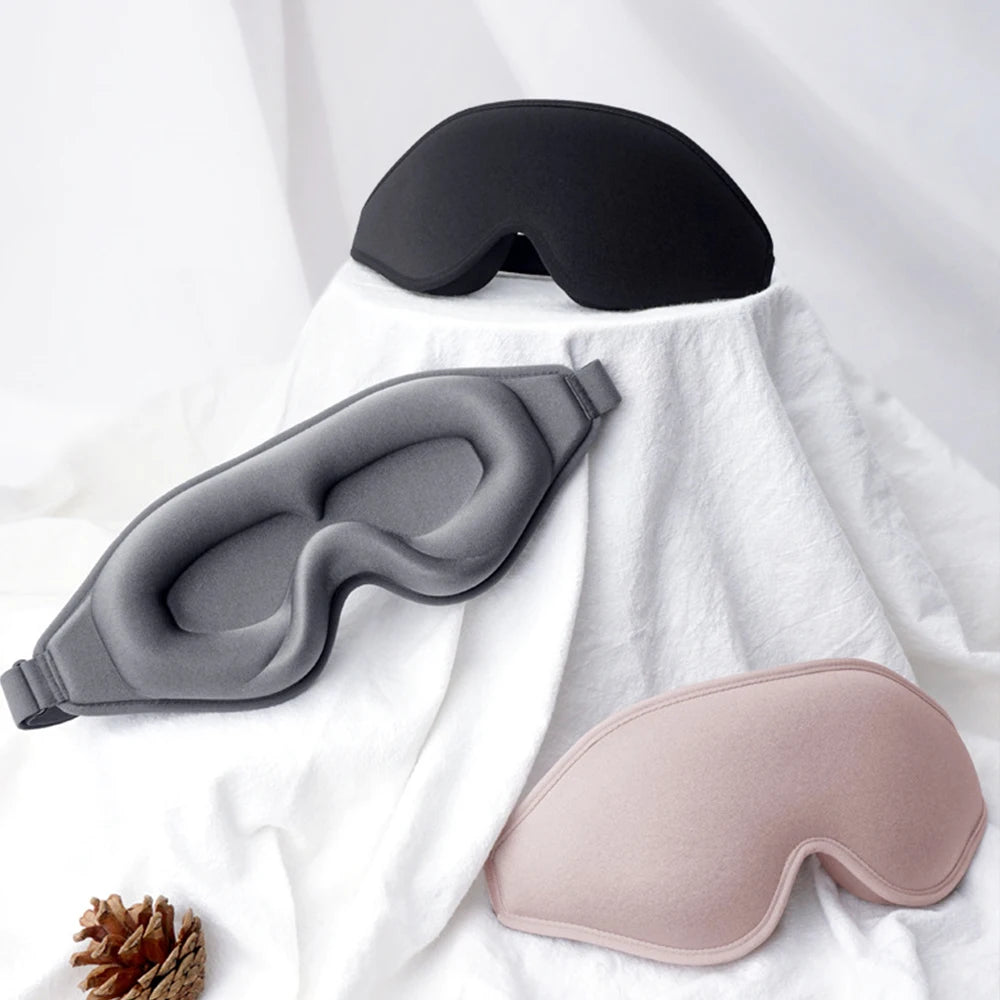 Three variety of coloured sleep masks in black, gray, and pink on a white fabric background.