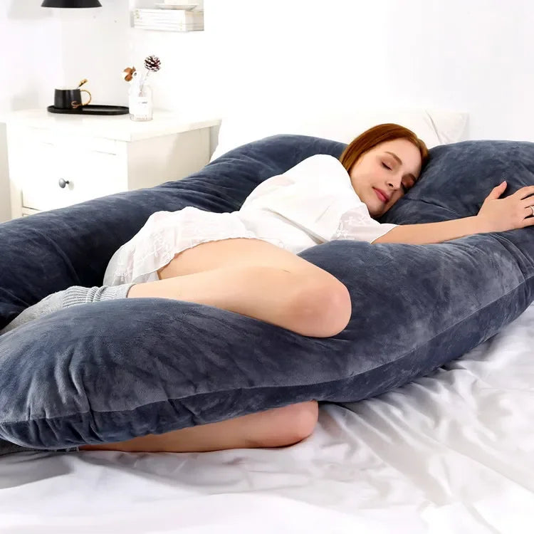 Pregnant maternity woman lying sideways on a large U-shaped body pillow in a bedroom.