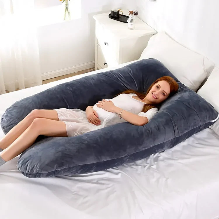 Pregnant maternity woman lying comfortably on a grey large U-shaped body pillow in a bedroom.