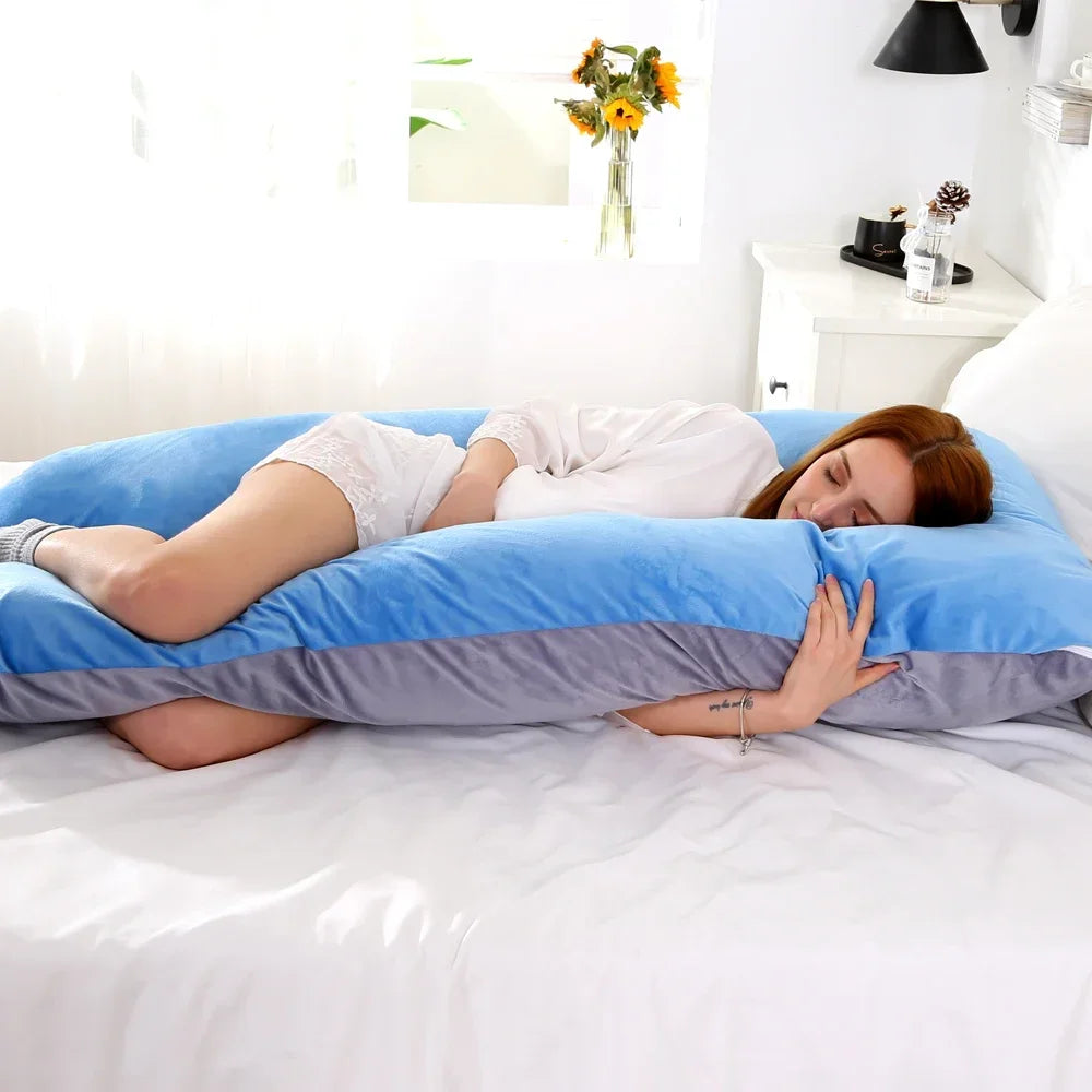Pregnant maternity woman lying on a large blue colour U-shaped body pillow in a bedroom.