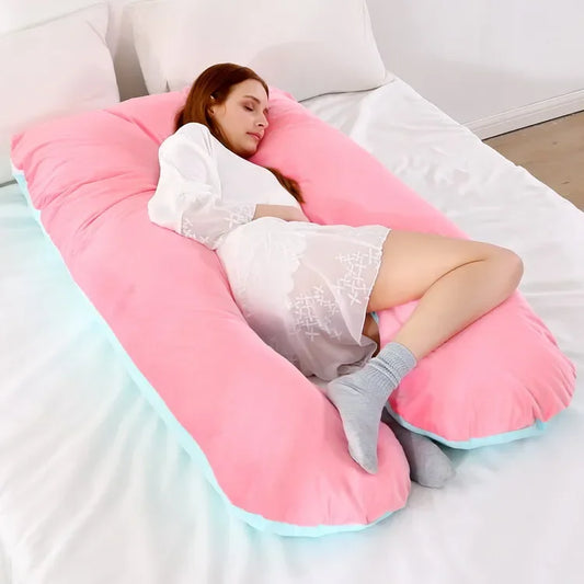 Pregnant maternity woman lying comfortably on a large pink U-shaped body pillow on a bed.