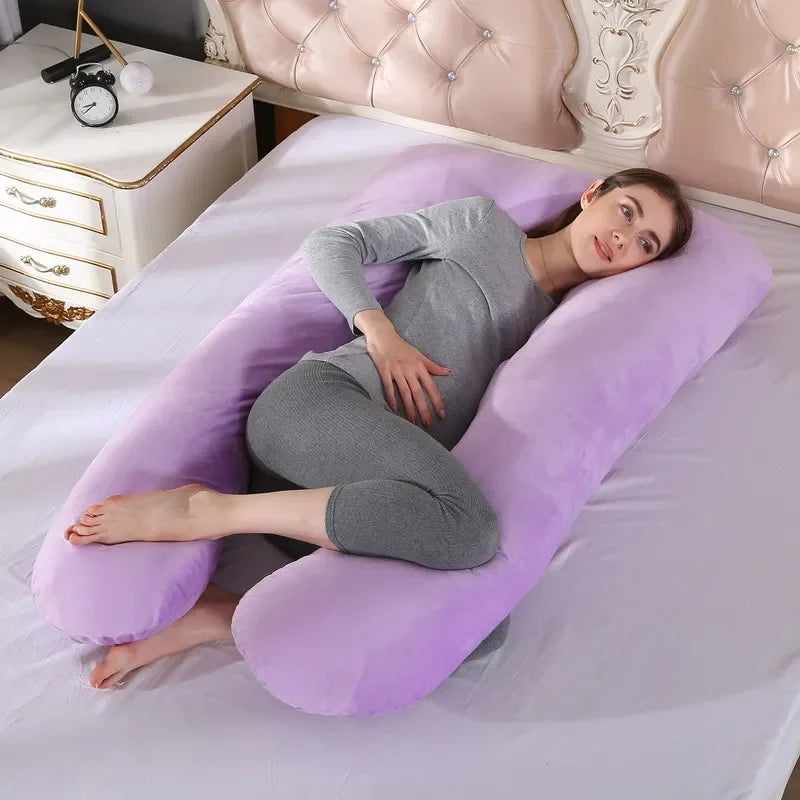 Pregnant maternity woman lying on a U-shaped purple pregnancy pillow in a bedroom.