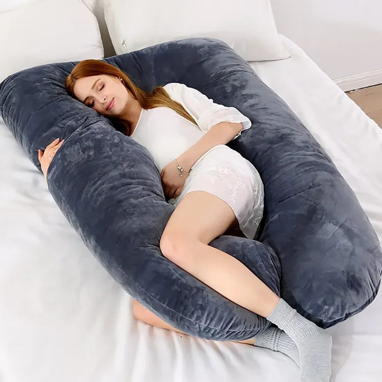 Pregnant maternity woman lying on a grey large U-shaped body pillow on a bed.