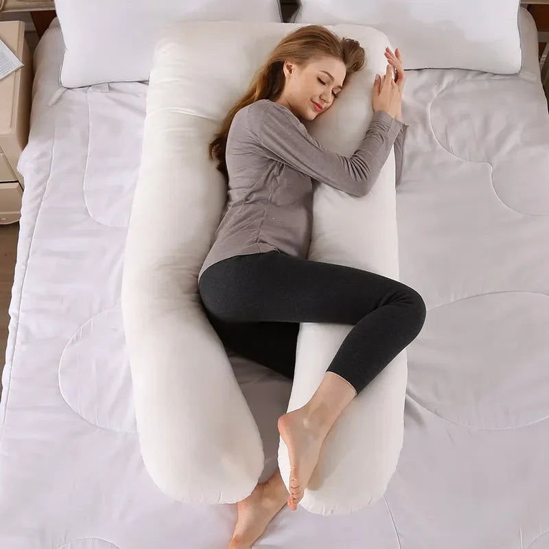 Pregnant maternity woman lying comfortably sideways on a white U-shaped body pillow in a bedroom.