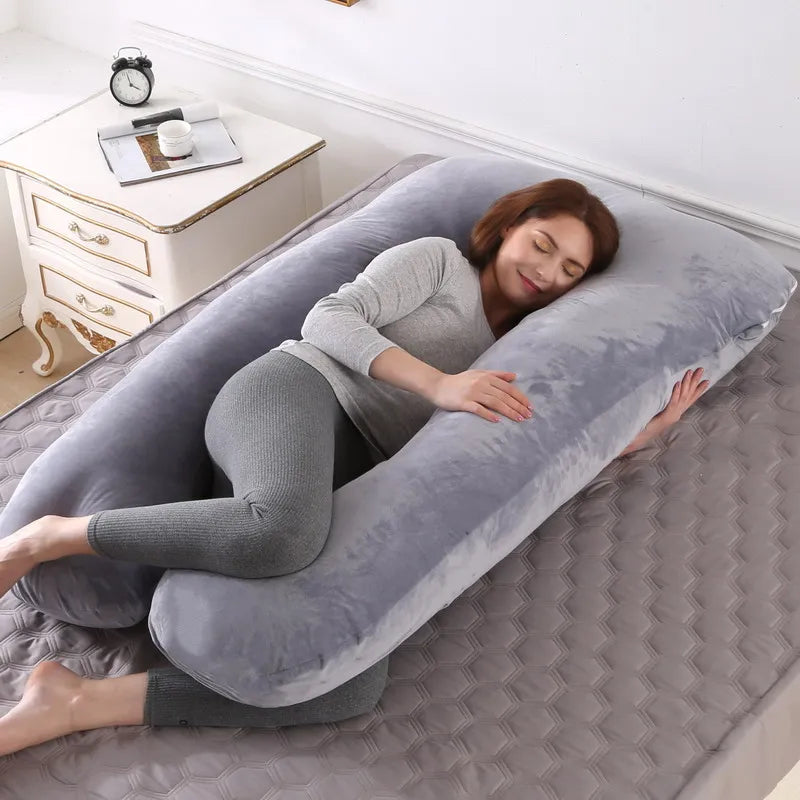 Pregnant maternity woman lying on a large grey U-shaped body pillow sleeping comfortably in the bedroom.