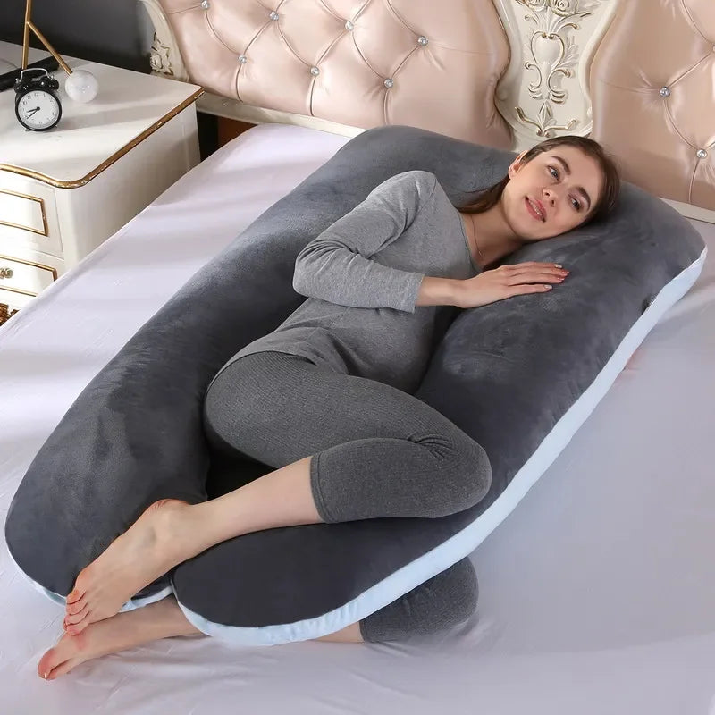 Pregnant maternity woman lying on a dark grey U-shaped body pillow in a bedroom.