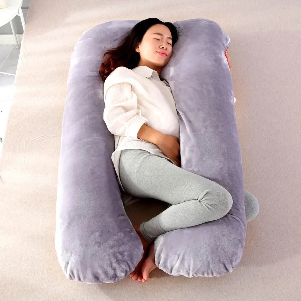 Pregnant maternity woman lying sideways on a grey U-shaped body pillow in a bedroom.