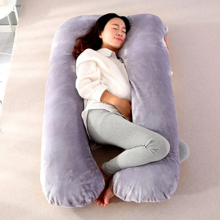 Pregnant maternity woman lying sideways on a grey U-shaped body pillow in a bedroom.