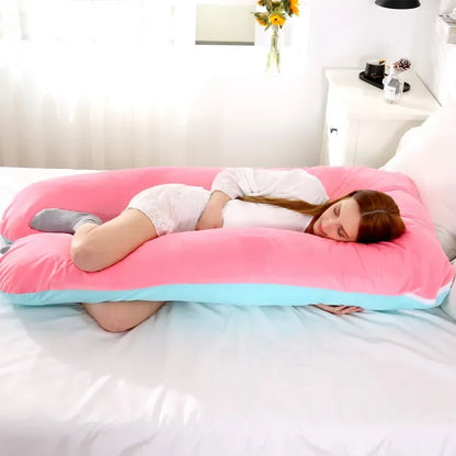 Pregnant maternity woman lying on a pink and blue large U-shaped pillow in a bedroom.