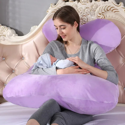 Mother holding a baby while sitting on a U-shaped purple pillow in a bedroom. Easy carrying baby.