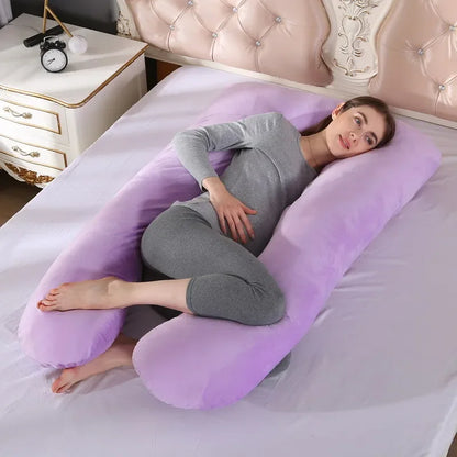 Pregnant maternity woman lying on a U-shaped purple pregnancy pillow in a bedroom.