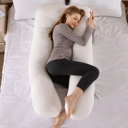 Pregnant maternity woman lying comfortably sideways on a white U-shaped body pillow in a bedroom.