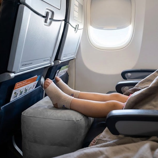 Child sitting in an airplane seat with feet up on the footrest, wearing socks.