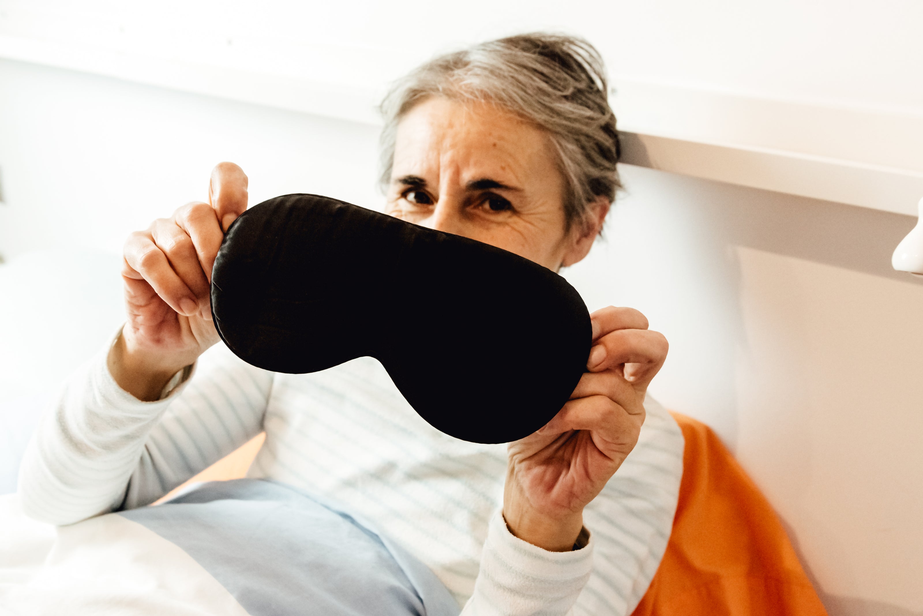 Woman resting on bed holding a sleeping mask.